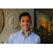 young man, Jonathan Ceja, standing near inside wall with dark hair and button down shirt smiling at camera